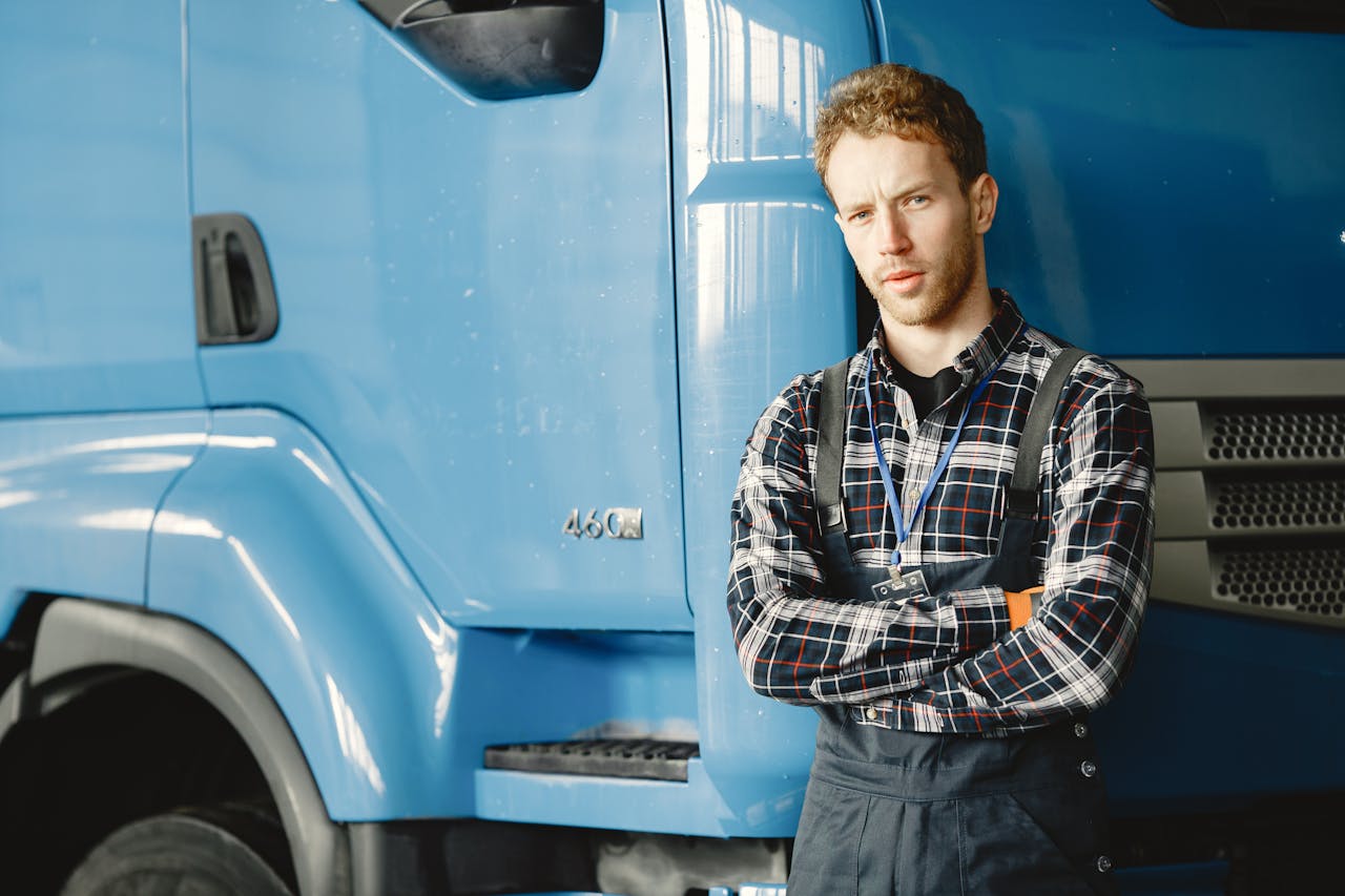 Auto mechanic with crossed arms posing by a blue truck in a garage